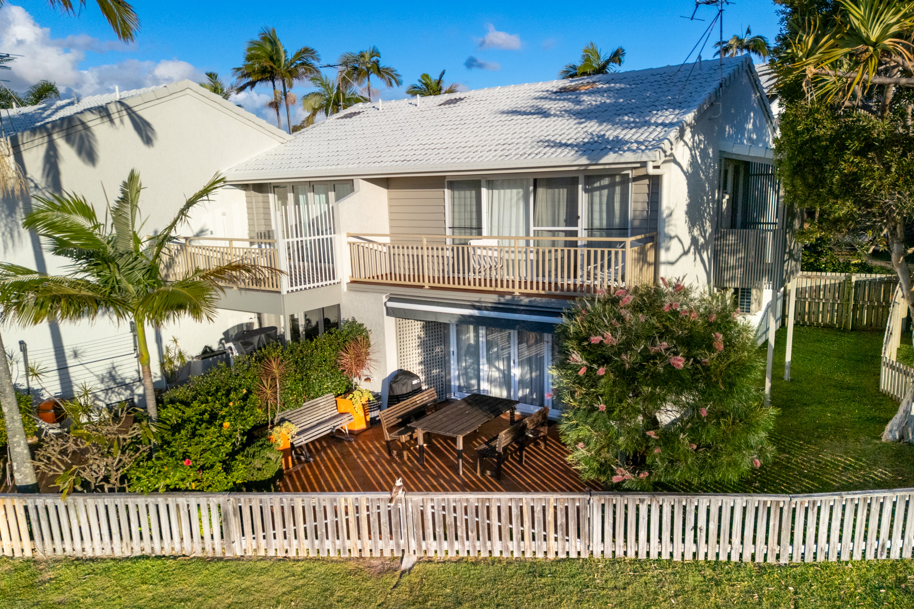 A two storey villa at Pandanus Palms Resort behind a white picket fence, framed by tall palms