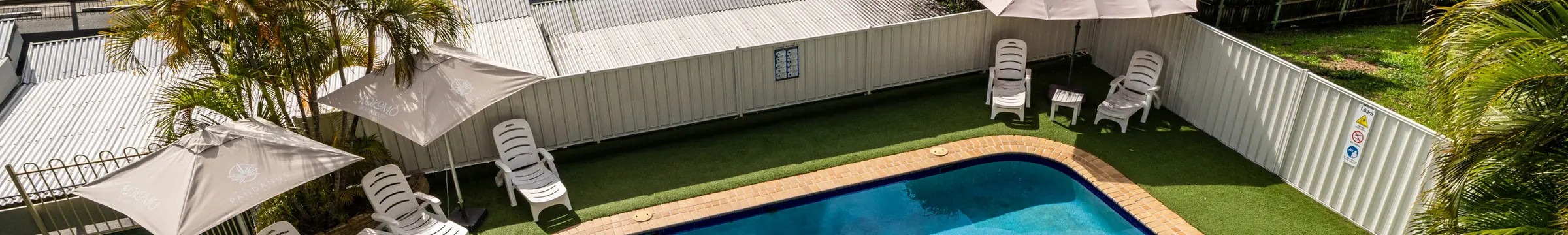The swimming pool at Pandanus Palms Resort, edged with lawn, sun lounges and umbrellas