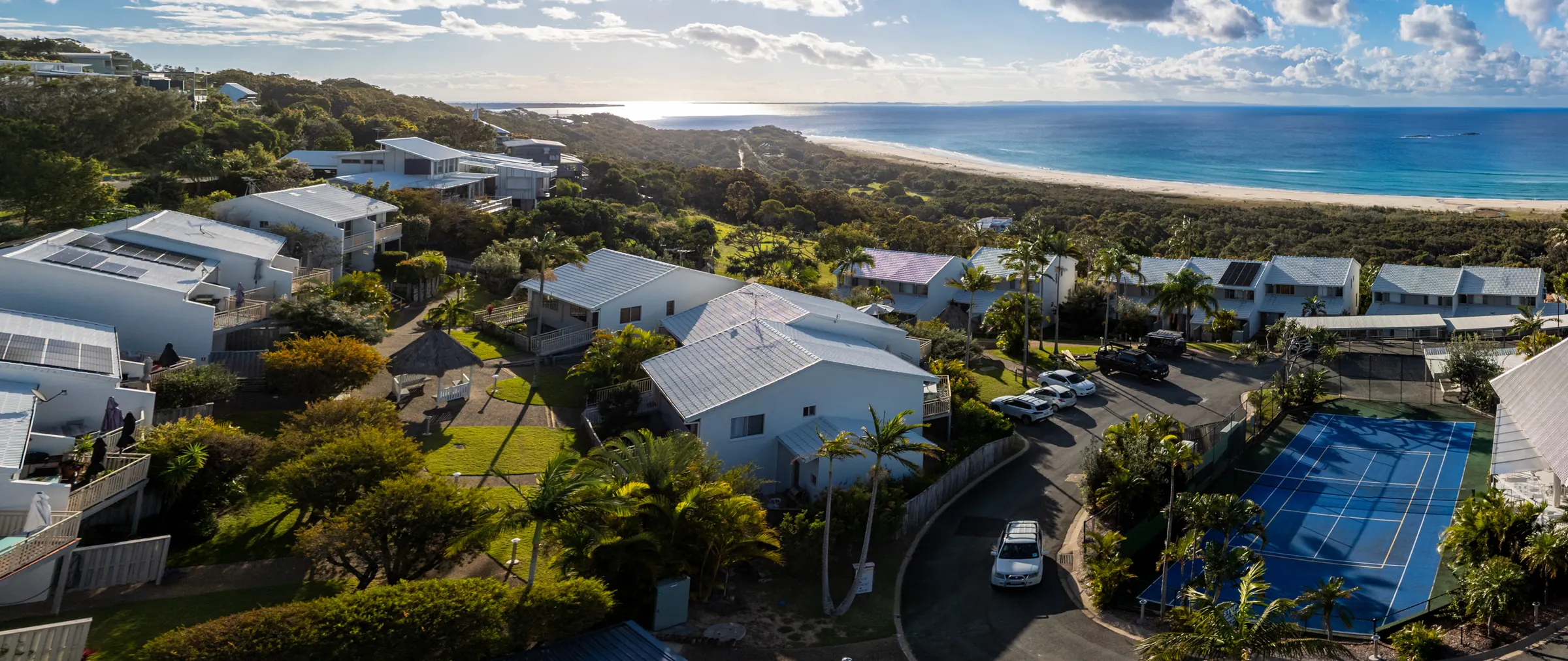 Panorama over Pandanus Palms Resort showing the villas, the tennis court and the beach curving away beyond