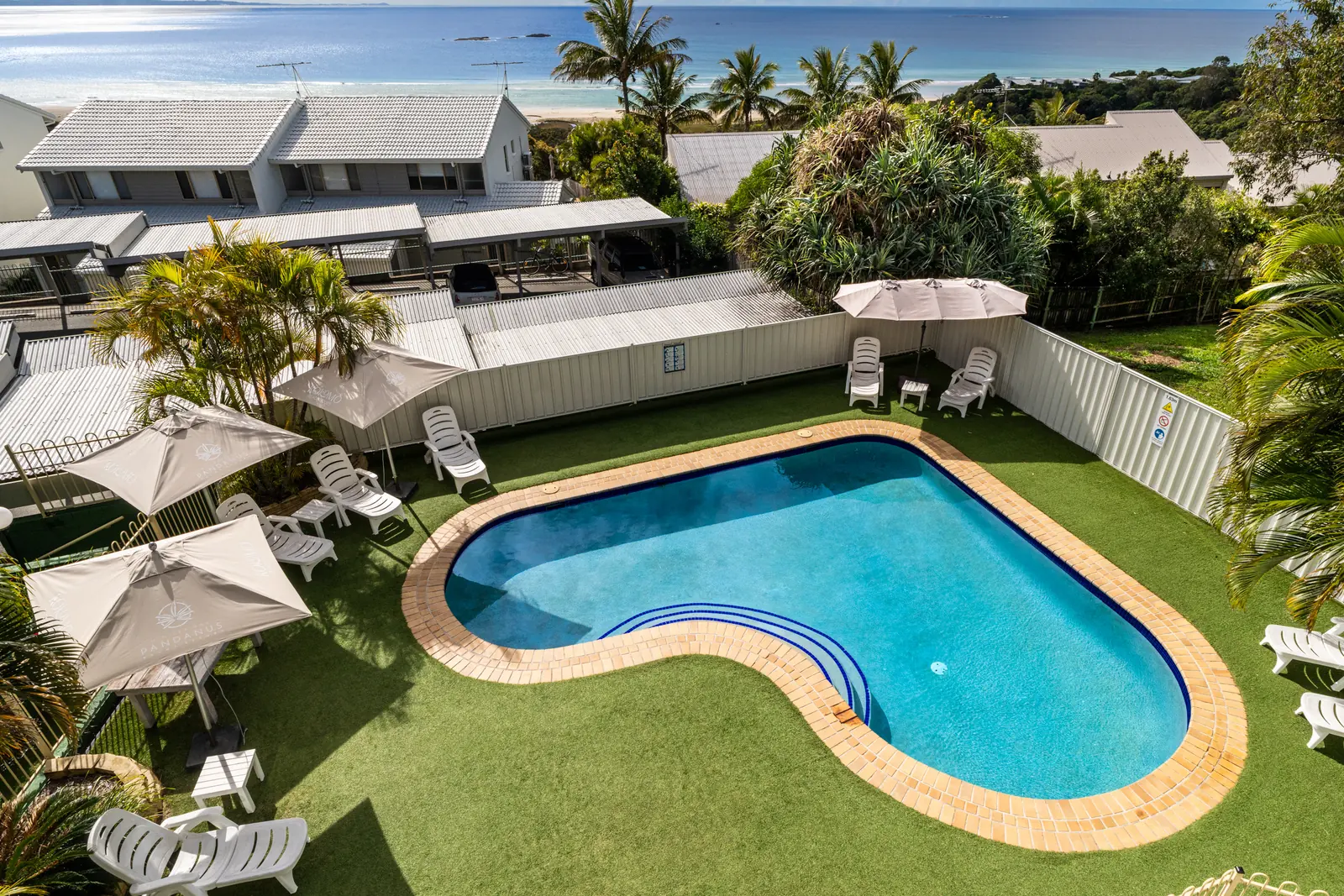 The swimming pool at Pandanus Palms Resort, edged with lawn, sun lounges and umbrellas, with the ocean in the distance