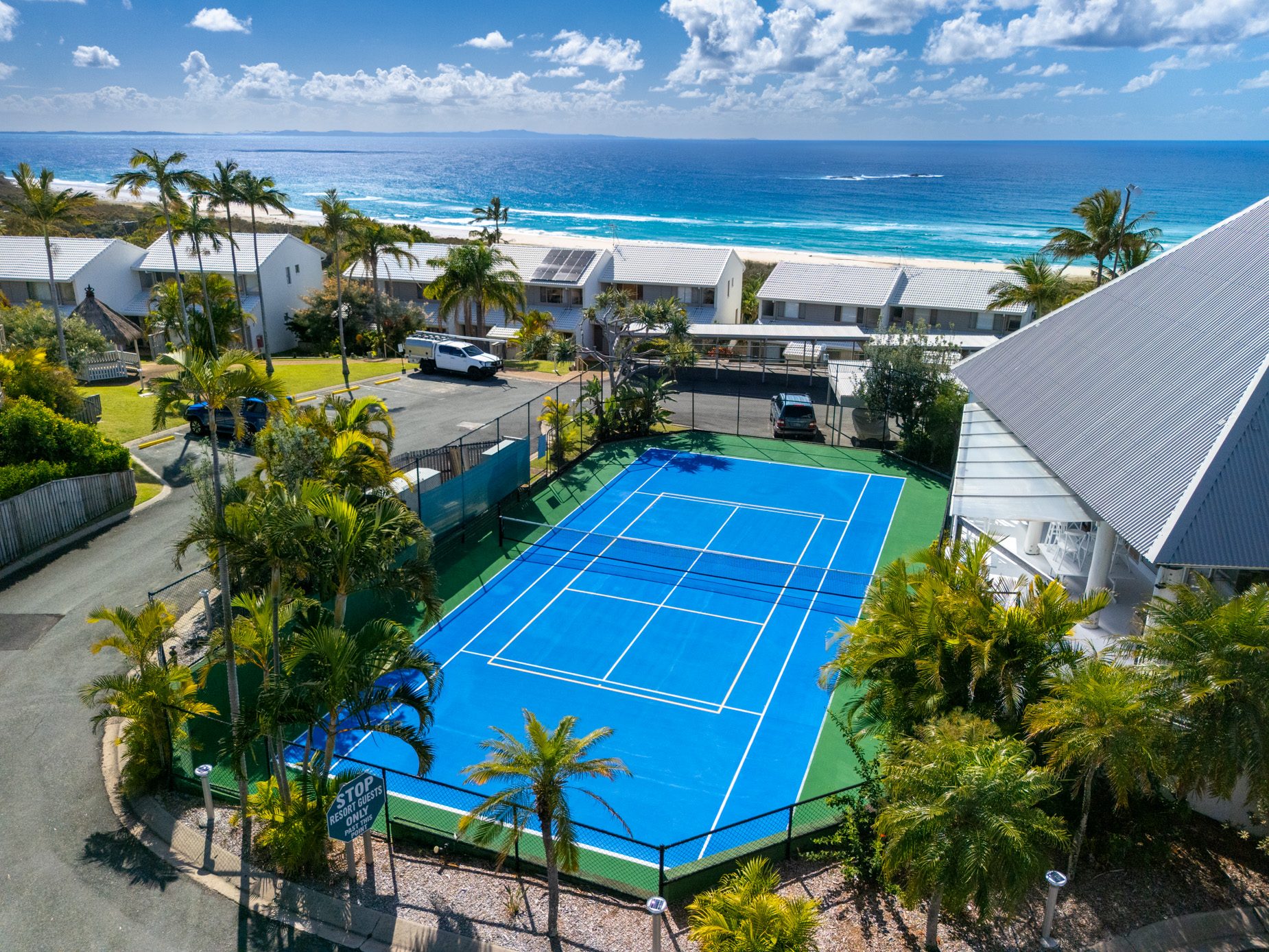 The tennis and pickle ball court at Pandanus Palms Resort from above, with the villas and the ocean beyond