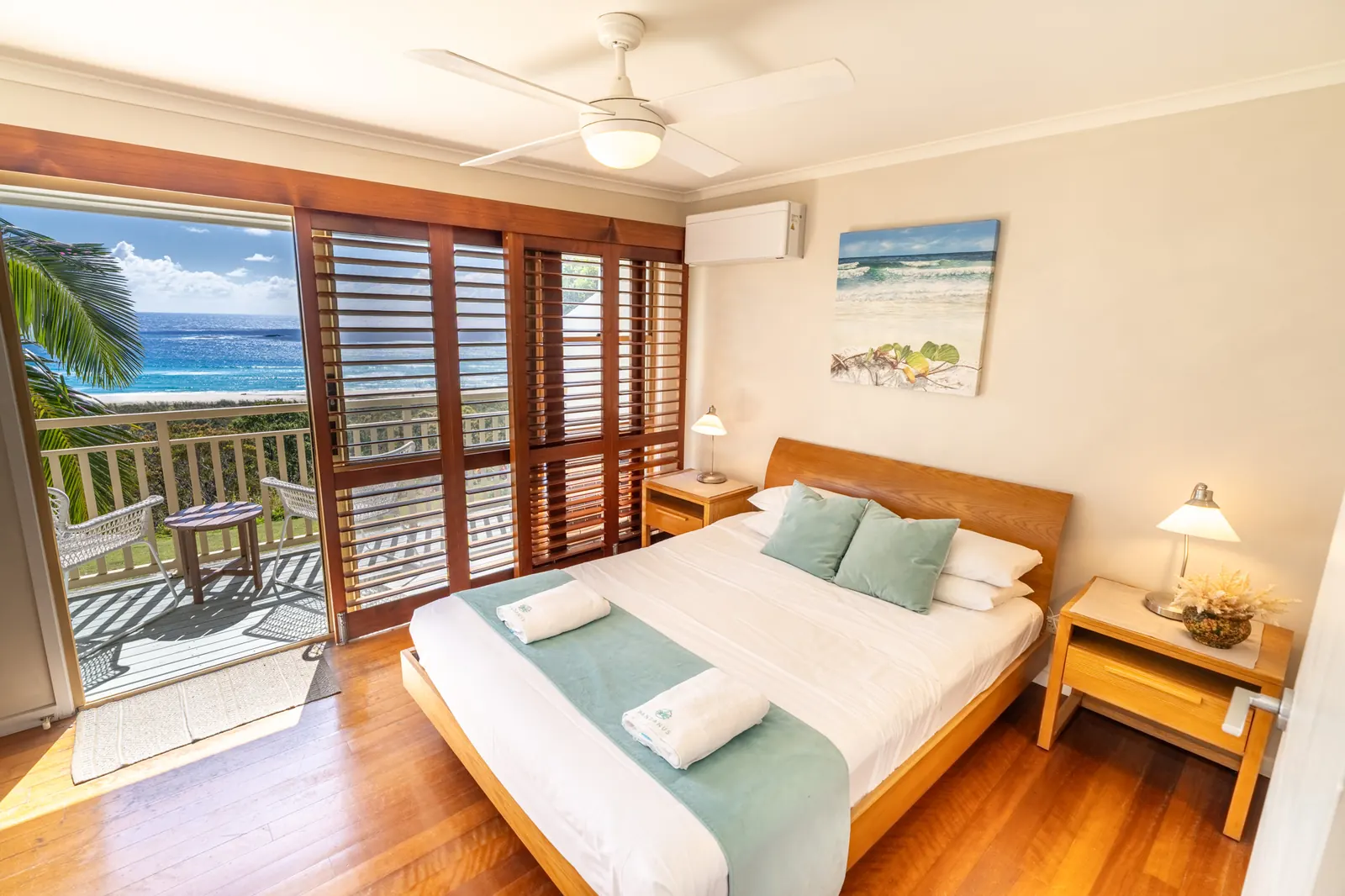 A bedroom with doors open to the balcony and the ocean beyond, in a Prestige Headland Ocean villa